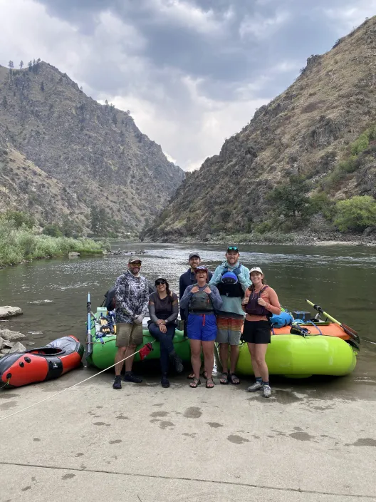 A group of slightly disheveled scientists stand in front of rafts and gear.