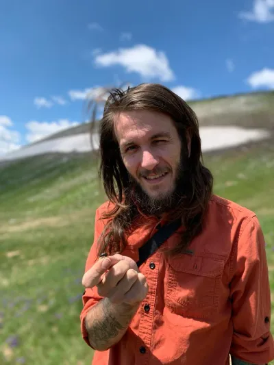 Cody standing outside in North Macedonia during his PhD holding Calosoma (Callisthenes) relictum specimen