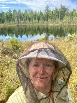 headshot of Jessie Lanterman Novotny standing in field and wearing hat with mosquito netting