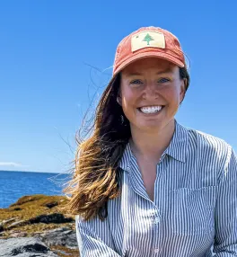 head and shoulders shot of Heather Glon in ball cap in front of a coastline on clear day